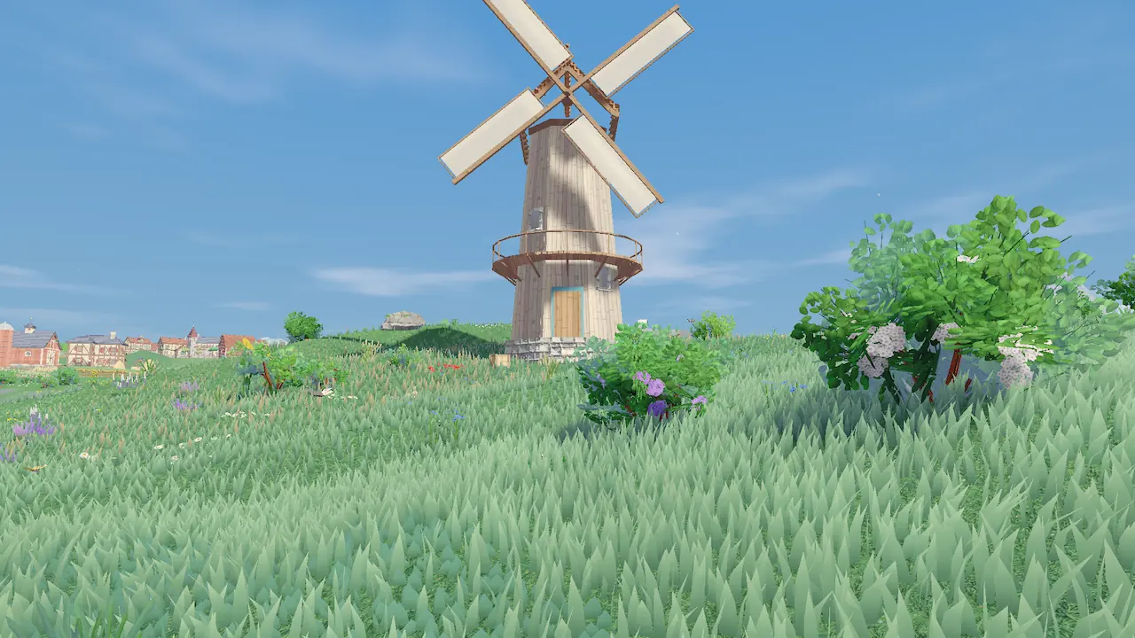 A tall windmill standing on a grassy rise against a clear blue sky, with flowering bushes nearby.